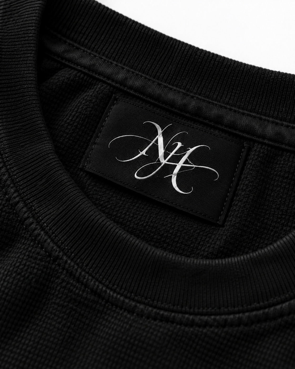 Close-up of the NH monogram label inside the ribbed collar, on black waffle knit